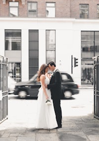 a bride and groom standing in front of a gate in london